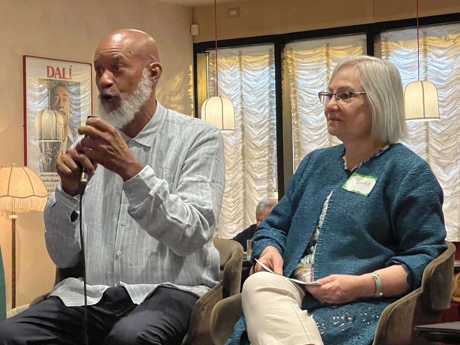 David seated and speaking into a microphone beside another participant.