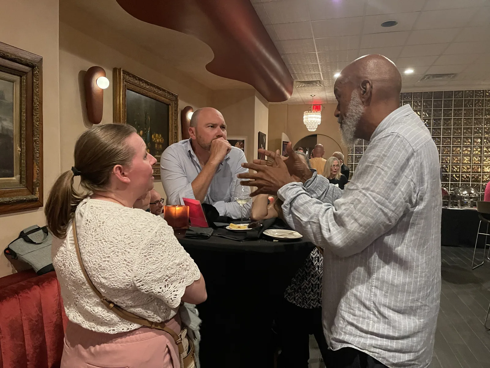 David gesturing in conversation with two people gathered around a table.