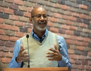 David speaking into a microphone against a brick wall.