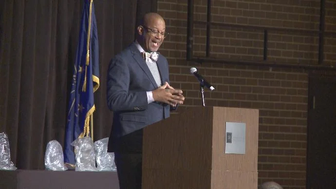 David speaking on a stage with a dark curtain behind him.